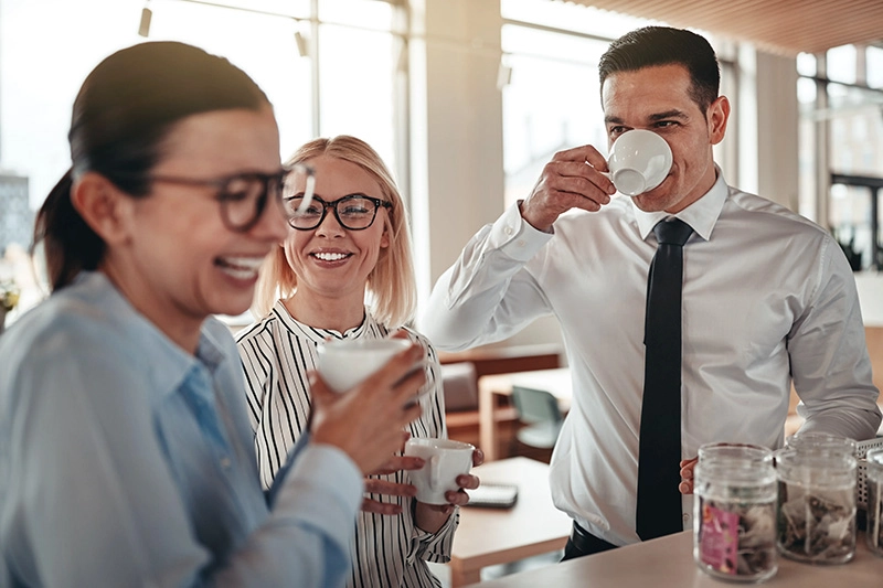 Drei Kollegen genießen gemeinsam Kaffee an einer Kaffeestation im Büro