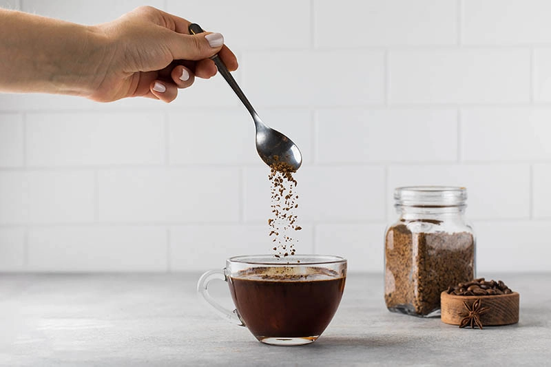 Instantkaffee wird mit einem Löffel in eine Glastasse gegeben