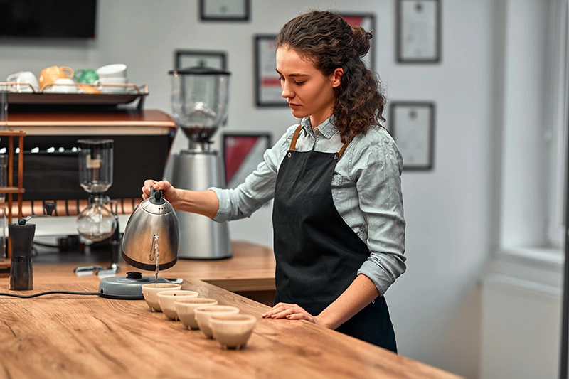 Barista gießt heißes Wasser für eine professionelle Kaffeeverkostung in kleine Tassen