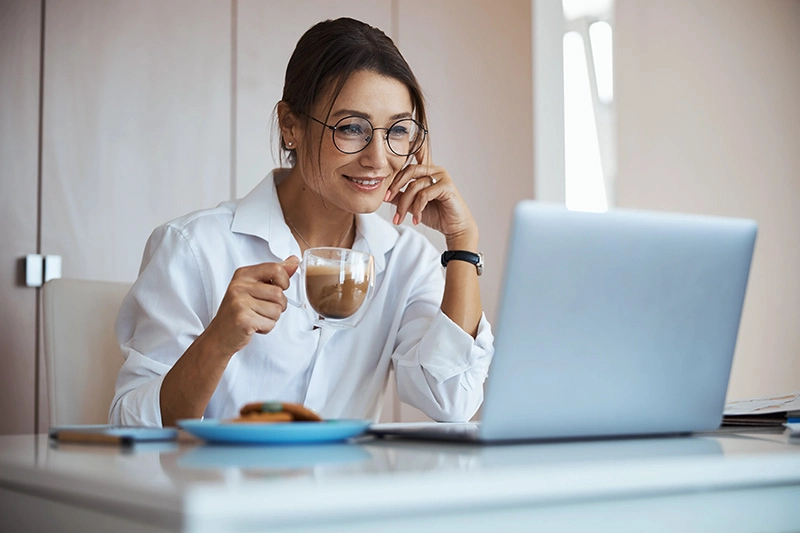 Frau trinkt Cappuccino im Homeoffice neben einem Laptop